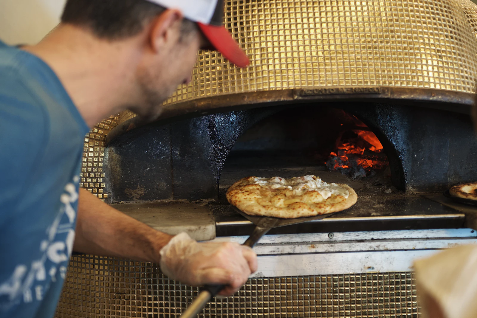 Le pizzaiolo enfourne une pizza dans le four à bois